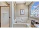 White bathtub in a light-brown bathroom with tiled walls, a window, and glass shower doors at 1655 Hermosa Dr, Highlands Ranch, CO 80126