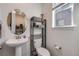 Cozy powder room with a pedestal sink, oval mirror, decorative shelving, and natural light from the window at 15624 W Floyd Dr, Morrison, CO 80465