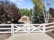 View of the property through a white wooden gate, showcasing the driveway and garage at 6449 E 163Rd Ave, Brighton, CO 80602