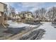 View of townhomes featuring attached garages, brick accents, and a small balcony, surrounded by trees in a snowy landscape at 1760 S Ammons St # D, Lakewood, CO 80232