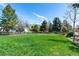 Spacious backyard featuring a lush lawn, mature trees, and a charming wooden fence under a beautiful blue sky at 2912 Lake Park Way, Longmont, CO 80503
