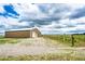 A tan barn with a gravel driveway, fenced yard, and metal roof at 73 N Dutch Valley Rd, Bennett, CO 80102