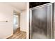 Hallway with a glimpse of a sunlit bedroom, leading to the bathroom with a glass shower door at 73 N Dutch Valley Rd, Bennett, CO 80102