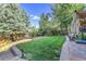 Lush backyard with a sprawling green lawn, mature trees, and a stone-lined flower bed at 2742 S Braun Way, Lakewood, CO 80228