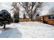 Snowy backyard with a wooden fence, mature trees, and a covered patio on a brick home at 768 W Larigo Ave, Littleton, CO 80120