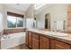 Well-lit bathroom featuring a vanity with double sinks, tub, and travertine tile at 12427 James Ct, Broomfield, CO 80020