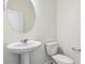 Bright half-bathroom with white fixtures, a pedestal sink, and a round mirror at 1038 Scotts Peak Dr, Berthoud, CO 80513