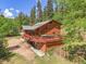 Exterior view of a cabin home with a large deck overlooking the lush greenery and surrounded by tall trees at 11182 S Barney Gulch Rd, Conifer, CO 80433