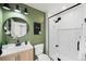 Modern bathroom with a walk-in shower, a wooden vanity, and green accent wall at 17767 E 54Th Ave, Denver, CO 80249