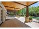Inviting covered patio with wood ceiling, stone columns, and views of the landscaped backyard and pool at 5 Churchill Dr, Cherry Hills Village, CO 80113