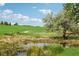 Lush green golf course landscape with pond, mature trees, and blue skies creates a serene and inviting environment at 16595 E 110Th Ave, Commerce City, CO 80022