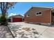 View of the brick house and detached garage with a red door and concrete driveway on a sunny day at 160 Northglenn Dr, Northglenn, CO 80233