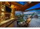 Inviting covered deck with a stone fireplace, TV, bar seating, comfortable furniture, and an outdoor grill at 7086 Esperanza Dr, Castle Pines, CO 80108