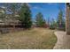 View of the backyard featuring a stone retaining wall, mature trees, and trampoline at 25312 E Glasgow Pl, Aurora, CO 80016