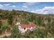 Aerial view of the property showcasing the white home with a red roof surrounded by dense trees at 11827 Brook Rd, Golden, CO 80403