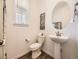 Well-lit powder room featuring a modern pedestal sink, toilet, and decorative mirror at 13261 E 110Th Pl, Commerce City, CO 80022