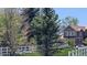 View of the gray home exterior behind the green trees with a white fence and lovely lawn at 7659 Lebrun Ct, Lone Tree, CO 80124