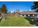 A home's large grassy backyard features a privacy fence, mature trees, and patio seating area at 90 Ammons St, Lakewood, CO 80226