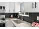 Close-up of the kitchen area with a stainless steel sink, white cabinetry, and a dark tile backsplash at 13438 E 13Th Pl, Aurora, CO 80011