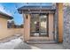 Exterior view of the house's tan wall and stone trim, and patio featuring bistro lights and glass doors at 1803 Avenida Del Sol, Castle Rock, CO 80104