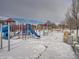 Community playground with slides and climbing structures surrounded by snow and bare trees at 17991 E 103Rd Ave, Commerce City, CO 80022