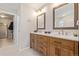 Bathroom with double sinks, wood cabinets, large mirrors, and a door leading to a walk-in closet at 12510 Fisher St, Englewood, CO 80112