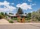 Single story home with brick and sage green exterior surrounded by colorful landscaping and mature trees at 10400 W 35Th Pl, Wheat Ridge, CO 80033