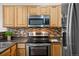 Close-up of the kitchen with stainless steel appliances, wood cabinets, and stylish backsplash for a modern culinary experience at 4674 Flower St, Wheat Ridge, CO 80033