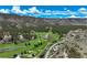 An aerial perspective of a lush golf course and rolling hills, showcasing trees, fairways, and mountains at 7134 Kiowa Rd, Larkspur, CO 80118
