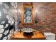 Rustic bathroom with brick wall, floral wallpaper, decorative mirror and vessel sink at 5886 Amber Ridge Dr, Castle Pines, CO 80108