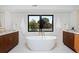 Symmetrical bright bathroom featuring a soaker tub, marble floors, wood cabinets, and a large window at 1374 S Vine St, Denver, CO 80210