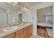 Bathroom featuring double sinks, tile countertops, wood cabinets, and a bedroom view at 15972 E Tall Timber Ln, Parker, CO 80134