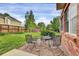 Back patio with a table and chairs, overlooking a fenced backyard with grass and landscaping at 3109 S Jebel Way, Aurora, CO 80013