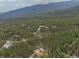 An aerial view shows several cabins nestled in a dense forest with the mountains in the distance at 509 Paiute Rd, Evergreen, CO 80439
