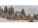 Charming log home featuring a stone chimney, balcony, and a snowy wooded setting at 11531 S Deer Creek Rd, Littleton, CO 80127