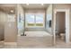 Bright bathroom featuring a soaking tub with tile surround and a window with plantation shutters at 17275 Gwilym Ct, Monument, CO 80132