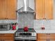 Kitchen stove with stainless steel hood, decorative backsplash, and modern appliances at 13804 W 61St Cir, Arvada, CO 80004