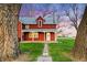 Red home with a covered porch framed by mature trees and green lawn with a stone pathway to the front door at 1805 W County Road 8, Berthoud, CO 80513