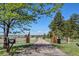 A long gravel driveway leads to a property, framed by wooden gates and lush greenery under a sunny sky at 40121 County Road 21, Elizabeth, CO 80107