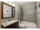 This bathroom features a vanity, toilet, medicine cabinet, and a shower and tub with gray tiles at 13778 W 71St Pl, Arvada, CO 80004