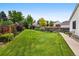 Large grassy backyard featuring lush landscaping, a wooden fence, and mature trees at 5656 S Sicily Ct, Aurora, CO 80015