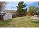 Spacious back yard featuring a large grassy area, mature trees, a wooden fence, and a storage shed at 11976 W Brandt Pl, Littleton, CO 80127