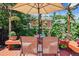 Backyard featuring a red wood deck with seating covered by an umbrella, a lush green lawn, and mature trees at 2311 W 46Th Ave, Denver, CO 80211