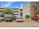 Condo building exterior with light gray siding, brick accents, balconies, parking lot, and nearby cars on a sunny day at 14214 E 1St Dr # B08, Aurora, CO 80011