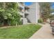 Exterior shot of a light gray condo building with well-maintained landscaping, sidewalk, and partial parking view at 14214 E 1St Dr # B08, Aurora, CO 80011