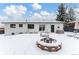 Backyard featuring a fire pit, seating, and a covered patio area against a backdrop of a well-maintained white brick house in winter at 12029 W Dakota Dr, Lakewood, CO 80228