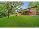 Spacious backyard featuring a lush lawn, mature trees, and a brick house with deck at 7077 Dudley Dr, Arvada, CO 80004