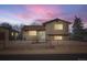 Two-story home with neutral siding, brown roof, gravel yard, chain-link fence, and colorful sky at 7611 Fernando Rd, Denver, CO 80221