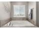 Relaxing soaker tub with neutral tile surround, window and modern art at 6707 6Th St, Frederick, CO 80530