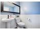 Bathroom with white pedestal sink, toilet, wainscoting, a dark-framed mirror, and light blue walls at 9745 Hummingbird Pl, Littleton, CO 80125